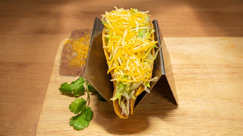 Hard shell taco with shredded cheese and lettuce, served with refried beans and cilantro.
