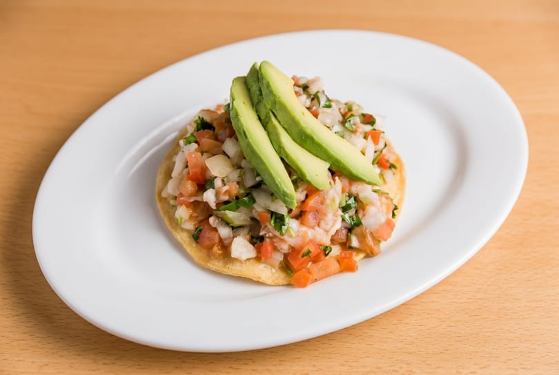 A tostada topped with ceviche, diced tomatoes, onions, cilantro, and avocado slices.