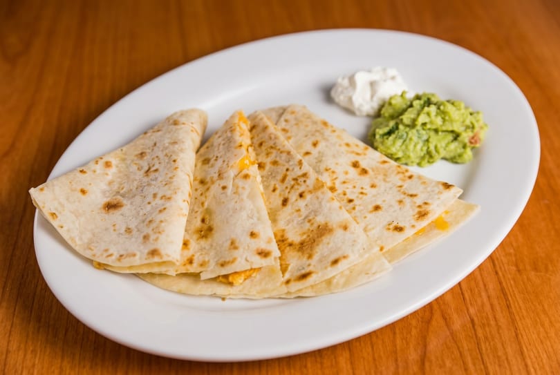 Cheese quesadillas with guacamole and sour cream on a white plate.